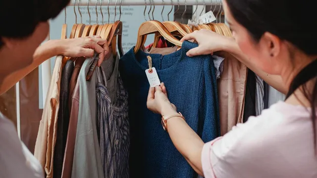 Two women browse clothes in a boutique, examining a blue dress.