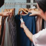 Two women browse clothes in a boutique, examining a blue dress.