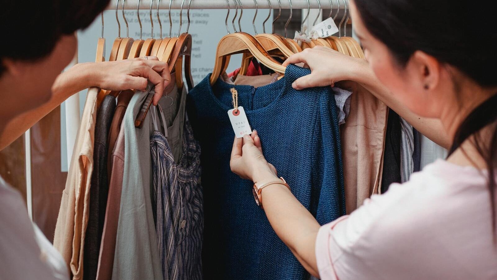 Two women browse clothes in a boutique, examining a blue dress.