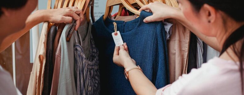 Two women browse clothes in a boutique, examining a blue dress.