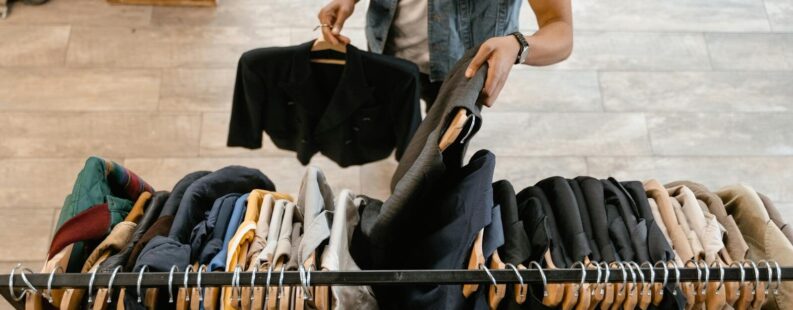 Person organizing secondhand fashion on a rack illustrating DPP resale and authenticated secondhand clothing
